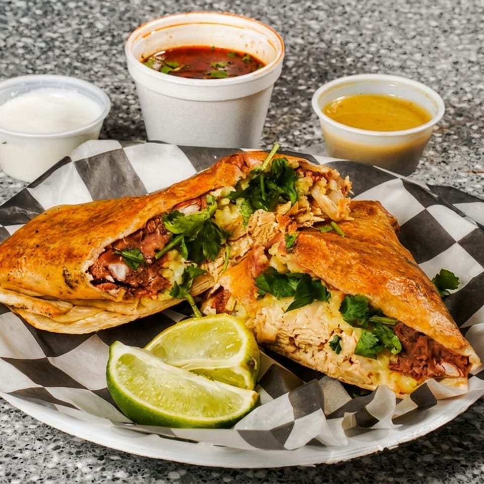 Two halves of a crispy burrito filled with meat and cilantro, with limes, sauces, and soup.
